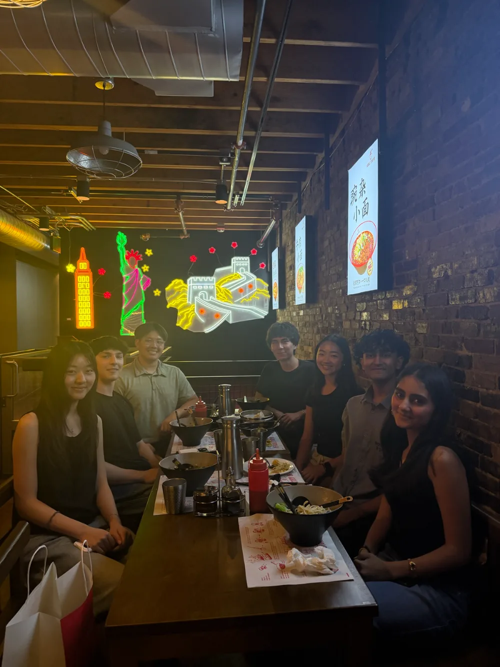 Seven people around a restaurant table with neon art on the back wall